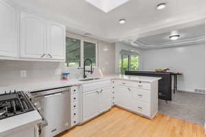 Kitchen with dishwasher, sink, light hardwood / wood-style flooring, and white cabinets