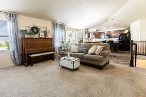 Carpeted living room with lofted ceiling, plenty of natural light, a chandelier, and a textured ceiling