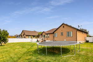 Back of house with a trampoline and a lawn