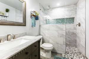 Bathroom featuring tiled shower, vanity, toilet, and tile walls