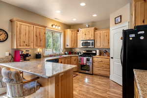 Kitchen with black appliances, kitchen peninsula, a kitchen breakfast bar, and light hardwood / wood-style floors