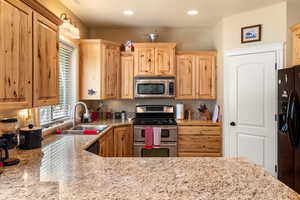 Kitchen featuring a wealth of natural light, sink, light stone countertops, and appliances with stainless steel finishes