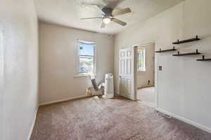 Unfurnished room with a textured ceiling, a healthy amount of sunlight, light carpet, and ceiling fan