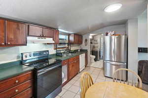 Kitchen with washer and dryer, lofted ceiling, stainless steel refrigerator, black electric range oven, and white dishwasher