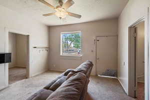 Living room with ceiling fan, light colored carpet, and a textured ceiling