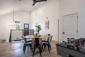 Dining room with high vaulted ceiling, ceiling fan with notable chandelier, and wood-type flooring