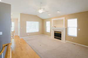 Unfurnished living room with light wood-type flooring, ceiling fan, lofted ceiling, and a tiled fireplace