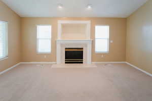 Unfurnished living room featuring plenty of natural light, a tiled fireplace, and light carpet