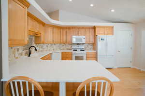 Kitchen with white appliances, light hardwood / wood-style flooring, kitchen peninsula, sink, and vaulted ceiling