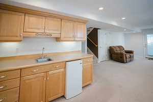 Kitchen with light brown cabinetry, dishwasher, light carpet, and sink