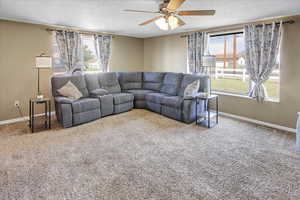 Carpeted living room with a textured ceiling, a healthy amount of sunlight, and ceiling fan