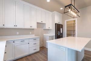 Kitchen featuring dark hardwood / wood-style floors, stainless steel fridge, decorative light fixtures, a center island, and white cabinetry