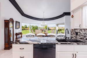 Kitchen featuring dishwasher, crown molding, sink, dark stone countertops, and white cabinets