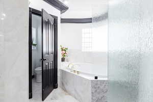 Bathroom featuring a textured ceiling, tiled tub, and toilet