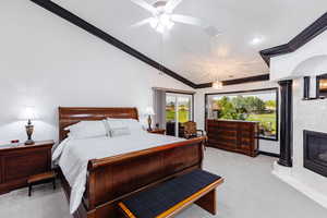 Carpeted bedroom featuring lofted ceiling, ceiling fan, a high end fireplace, and ornamental molding