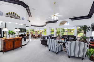 Living room with carpet flooring, ceiling fan, crown molding, and a high ceiling