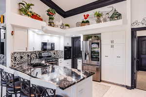 Kitchen with black appliances, white cabinetry, dark stone counters, and kitchen peninsula