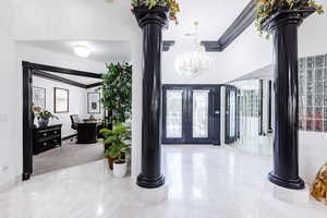 Entrance foyer featuring french doors, vaulted ceiling, an inviting chandelier, and decorative columns