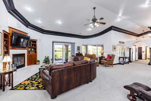 Living room featuring a fireplace, crown molding, light colored carpet, and ceiling fan