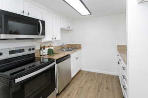 Kitchen with light wood-type flooring, stainless steel appliances, sink, light stone countertops, and white cabinets