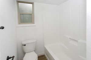 Bathroom with toilet, bathtub / shower combination, and wood-type flooring