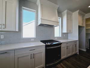 Kitchen with black range oven, light stone countertops, backsplash, and dark wood-type flooring