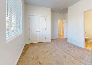 Unfurnished bedroom with ensuite bathroom, light colored carpet, and a closet