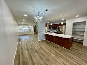 Kitchen featuring stainless steel appliances, light hardwood / wood-style flooring, a notable chandelier, kitchen peninsula, and pendant lighting