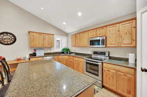 Kitchen with lofted ceiling, dark stone countertops, appliances with stainless steel finishes, and a breakfast bar area