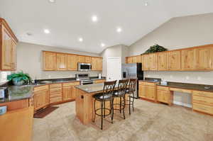 Kitchen featuring a kitchen island, a breakfast bar area, appliances with stainless steel finishes, high vaulted ceiling, and dark stone countertops