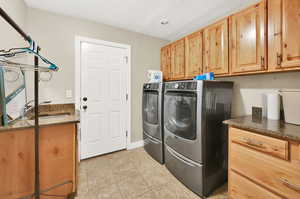 Clothes washing area featuring light tile patterned floors, sink, cabinets, washer and clothes dryer, and a textured ceiling