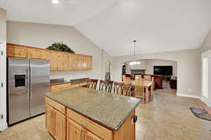 Kitchen featuring stone counters, a notable chandelier, a center island, hanging light fixtures, and stainless steel refrigerator with ice dispenser