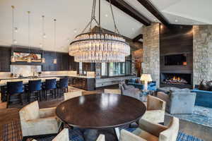 Dining area with dark hardwood / wood-style floors, a stone fireplace, sink, a chandelier, and vaulted ceiling with beams