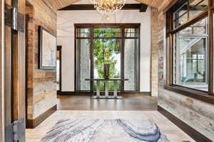 Entrance foyer with an inviting chandelier, wood-type flooring, vaulted ceiling with beams, and wooden walls