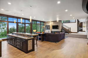 Kitchen with a fireplace, light hardwood / wood-style flooring, decorative light fixtures, stone countertops, and a breakfast bar