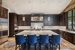 Kitchen with an island with sink, built in fridge, sink, and light stone counters