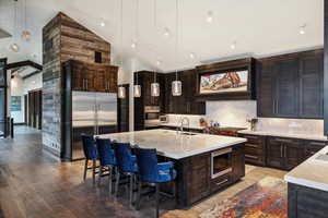 Kitchen with a center island with sink, light hardwood / wood-style floors, hanging light fixtures, stainless steel appliances, and high vaulted ceiling