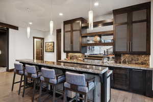 Kitchen with decorative light fixtures, backsplash, light stone counters, and light hardwood / wood-style floors