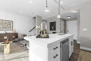 Kitchen with hanging light fixtures, sink, wood-type flooring, an island with sink, and stainless steel dishwasher