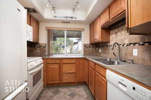 Kitchen featuring white appliances, sink, track lighting, a tray ceiling, and tile counters