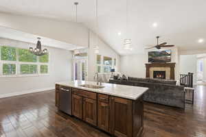 Kitchen with dark hardwood / wood-style floors, a tiled fireplace, ceiling fan with notable chandelier, hanging light fixtures, and sink