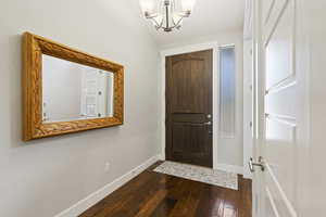 Foyer entrance featuring dark wood-type flooring, lofted ceiling, and an inviting chandelier