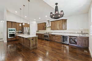 Kitchen with hanging light fixtures, beverage cooler, stainless steel appliances, and wall chimney range hood