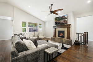 Living room featuring dark wood-type flooring, ceiling fan, high vaulted ceiling, and a tiled fireplace