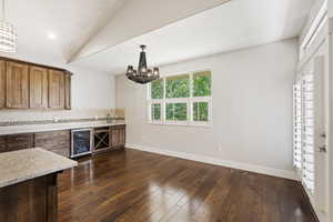 Kitchen featuring light stone countertops, a chandelier, dark hardwood / wood-style floors, beverage cooler, and pendant lighting