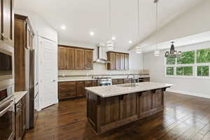 Kitchen with pendant lighting, a kitchen breakfast bar, an island with sink, dark wood-type flooring, and wall chimney exhaust hood