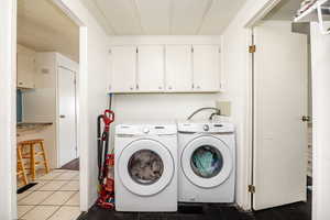 Laundry area featuring a textured ceiling, washing machine and dryer, cabinets, and light tile patterned floors