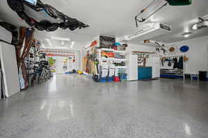 Tandem 3 car garage with epoxy flooring, cabinetry, workbench, and shelving.