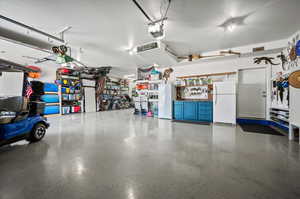 Tandem 3 car garage with epoxy flooring, cabinetry, workbench, and shelving.