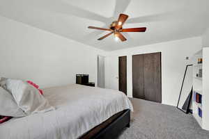 Carpeted bedroom with ceiling fan and two closets